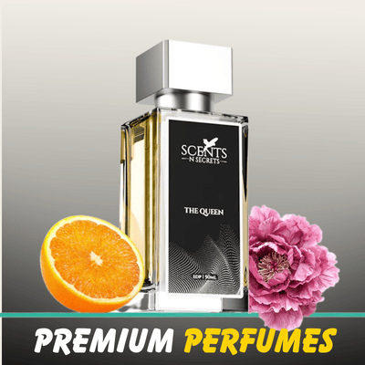 A 50ml bottle of "The Queen" Eau de Parfum by Scents N Secrets, flanked by a fresh orange slice and a pink peony flower.