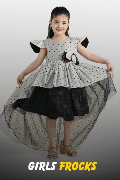 A young girl wearing a stylish black and white polka dot high-low party frock with a bow detail and layered tulle from Nazz Collections.